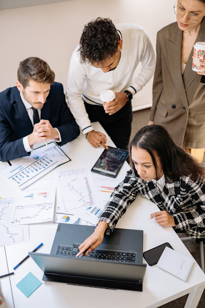 gallery-3 Team of colleagues discussing financial charts at a laptop in an office setting.